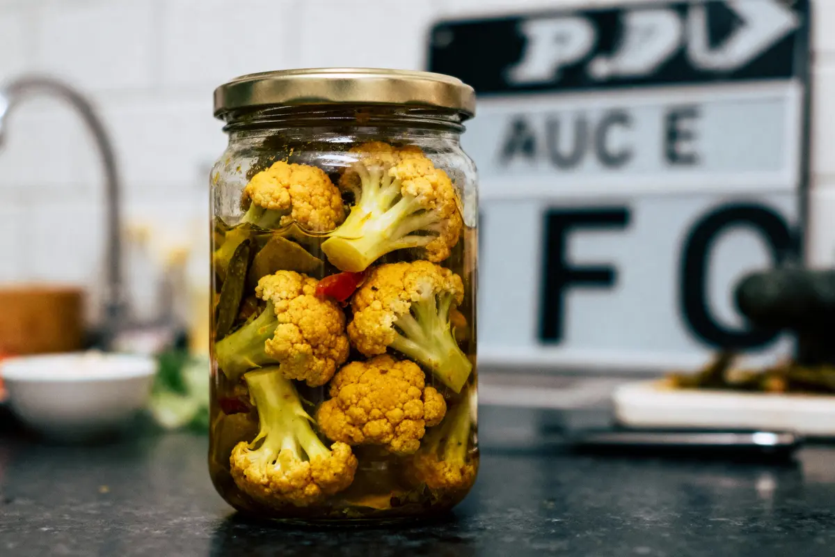 Pot de chou-fleur mariné sur comptoir de cuisine, avec panneaux flous en arrière-plan.