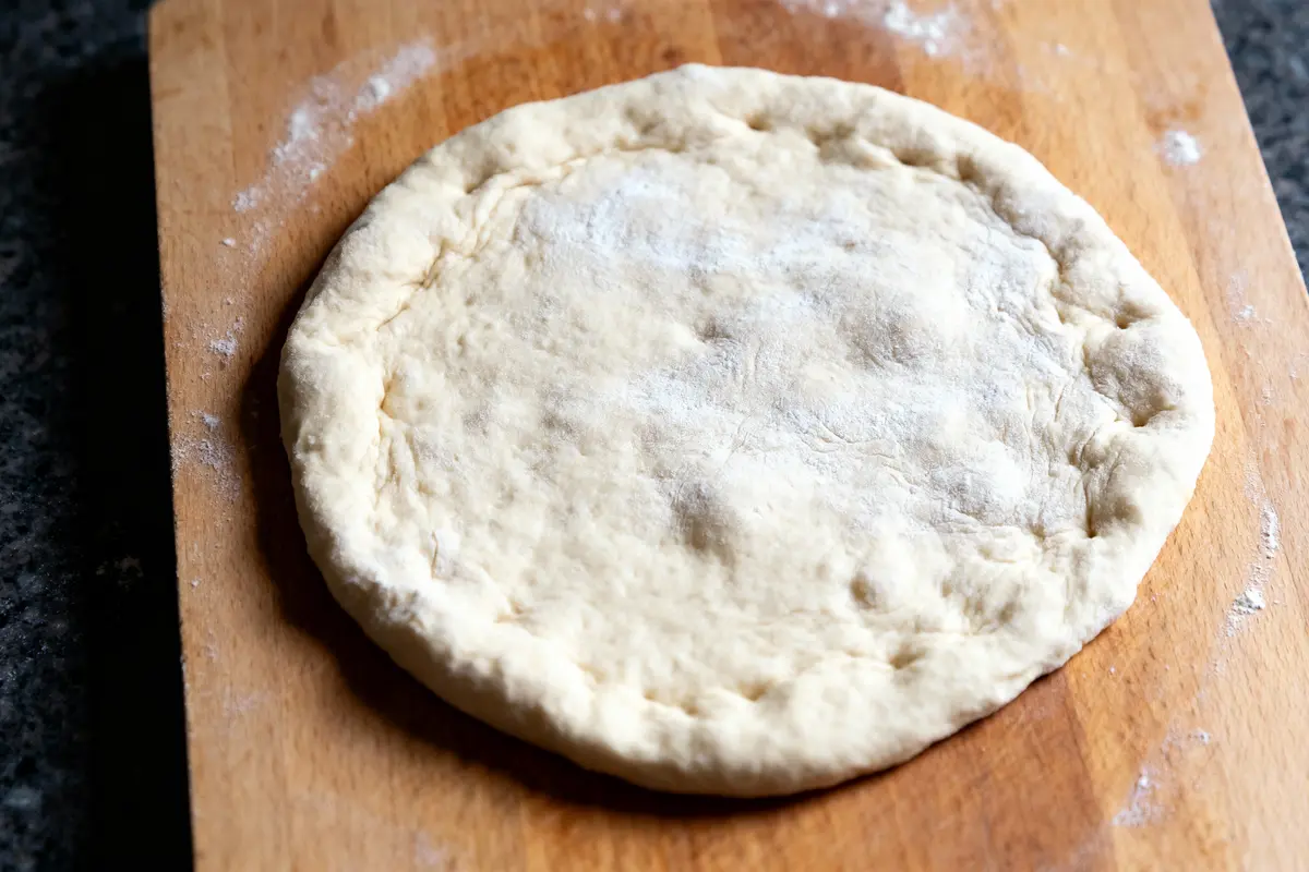 Pâte à pizza non cuite sur planche en bois enfarinée, vue de dessus.