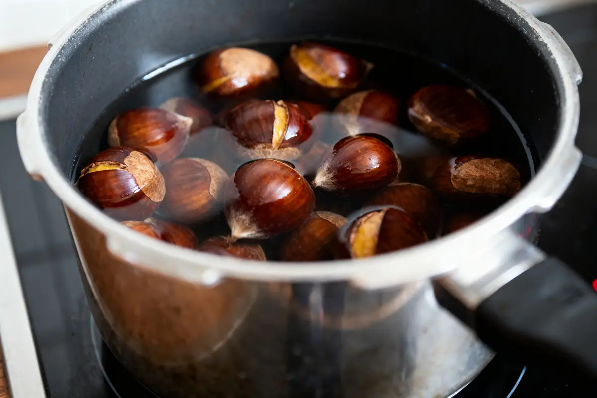 Châtaignes brunes bouillantes dans une casserole noire remplie d'eau, sur une cuisinière.