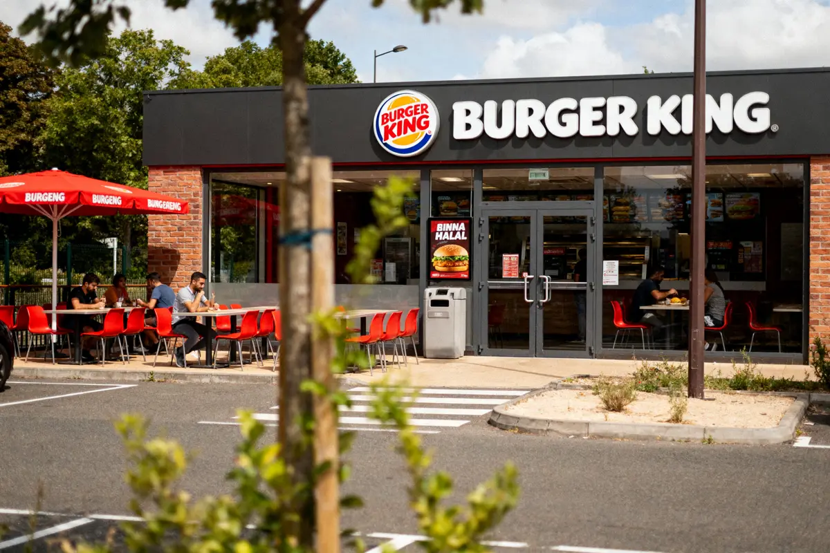 Façade d'un restaurant Burger King avec terrasse extérieure et clients assis, entouré de verdure.