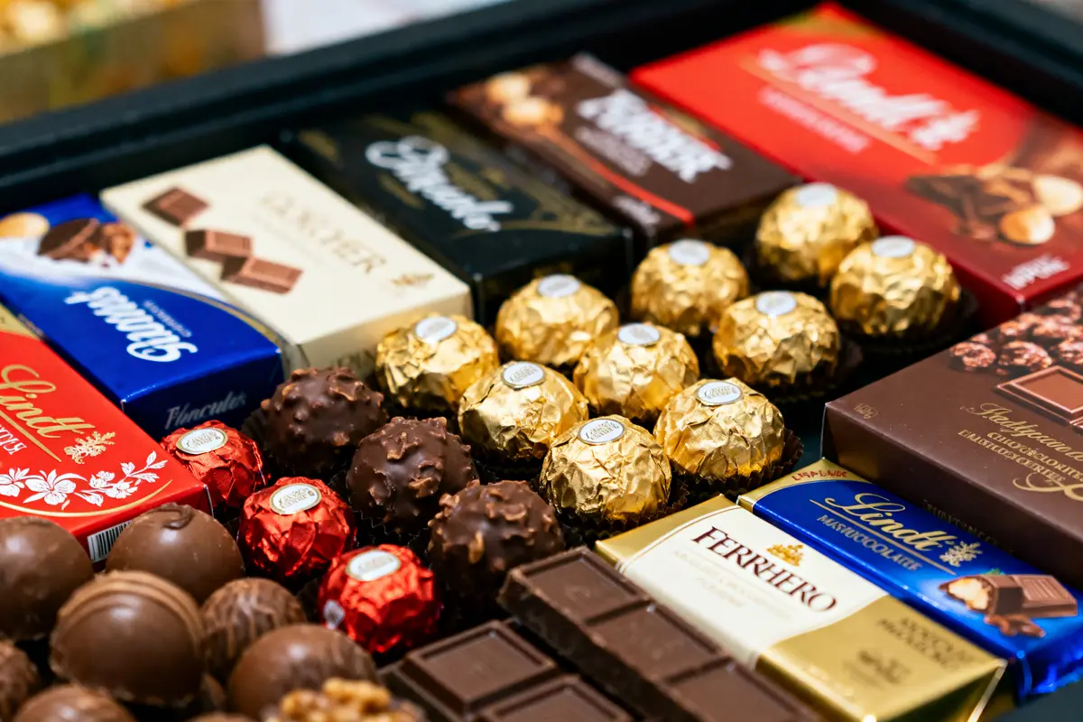 Assortiment de chocolats variés, incluant boîtes de marques connues et chocolats emballés individuellement en aluminium doré.