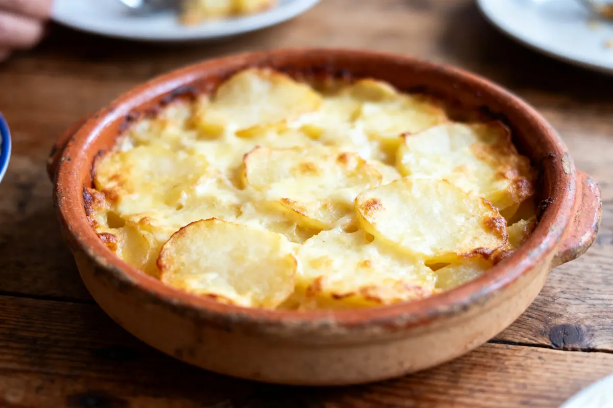 Plat de gratin dauphinois doré, dans un plat en terre cuite, sur une table en bois.