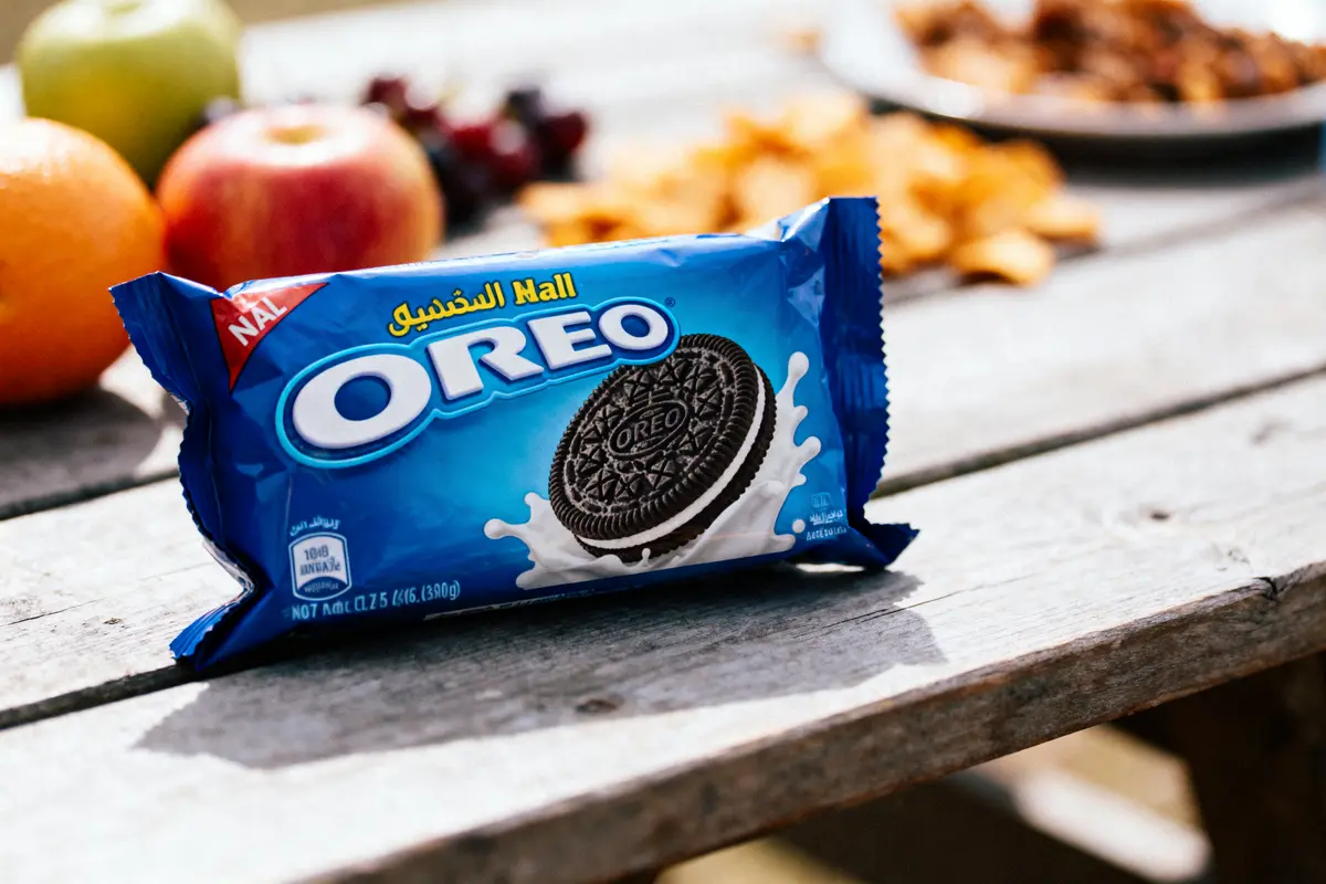 Paquet d'Oreo sur une table en bois, fruits en arrière-plan flou.