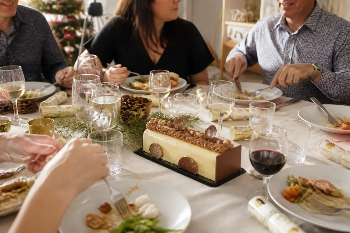 Des convives dînent avec une bûche de Noël en dessert, entourés de verres et décorations festives.