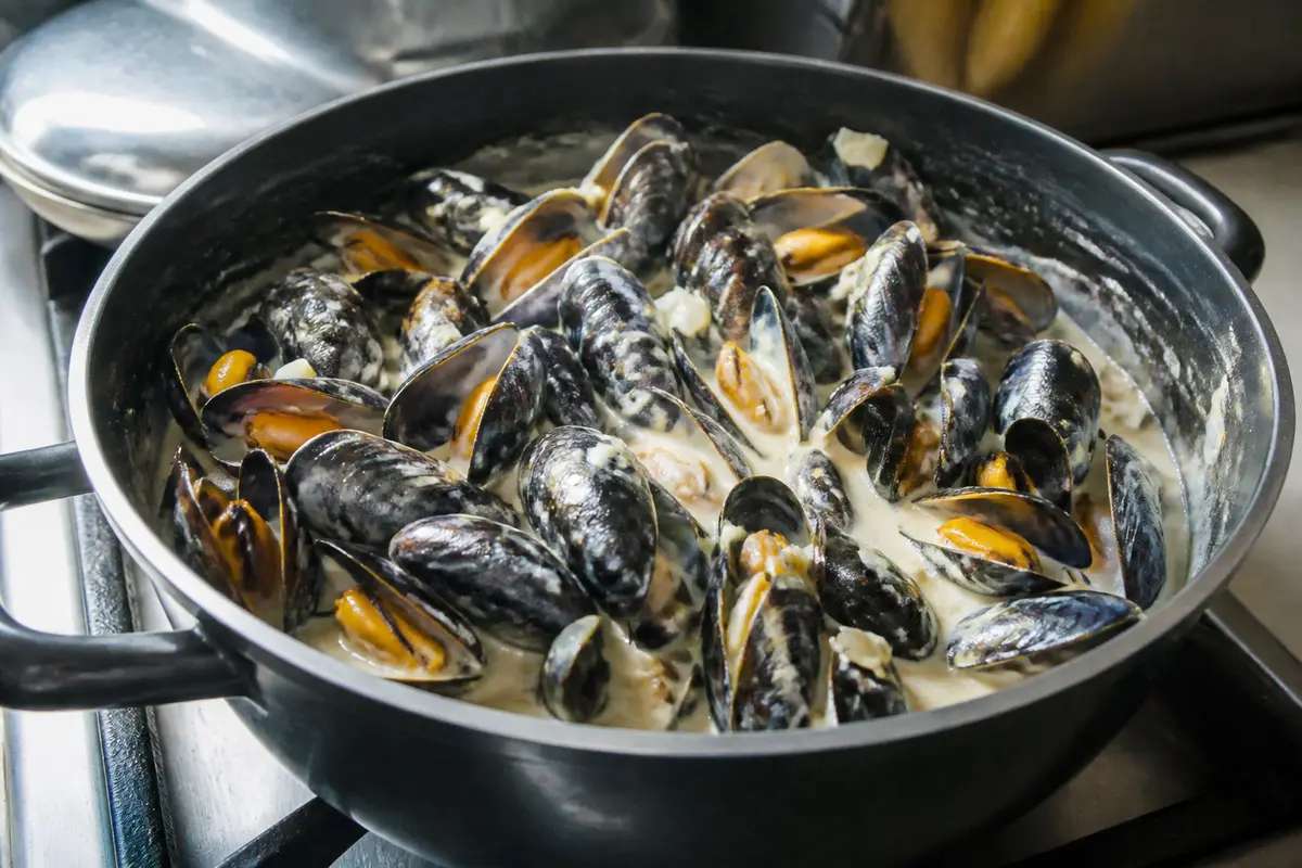 Grande casserole remplie de moules cuites dans une sauce crémeuse, posée sur une cuisinière.